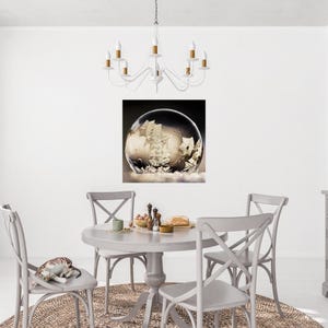 May include: A dining room scene featuring a round gray table and four matching chairs. A snow globe art print hangs on the wall. A white chandelier hangs above the table. A cat rests on one of the chairs.