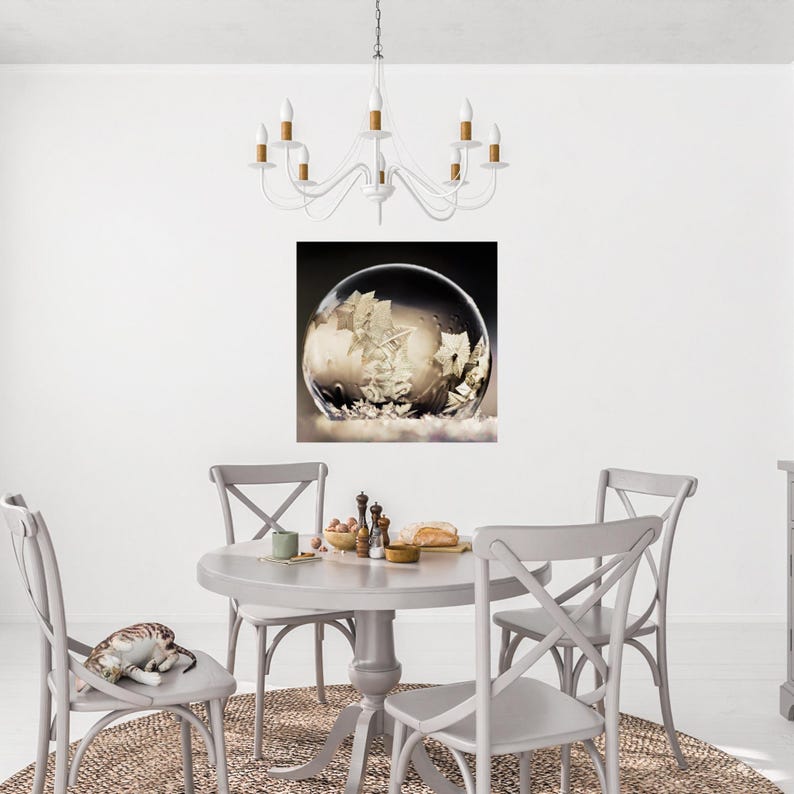 May include: A dining room scene featuring a round gray table and four matching chairs. A snow globe art print hangs on the wall. A white chandelier hangs above the table. A cat rests on one of the chairs.