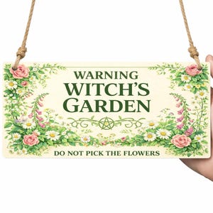 Peut inclure: Panneau rectangulaire en bois avec le texte "WARNING WITCH'S GARDEN" et "DO NOT PICK THE FLOWERS". Le panneau est orné de roses roses, de marguerites et d'autres fleurs. Il est suspendu à une corde naturelle.