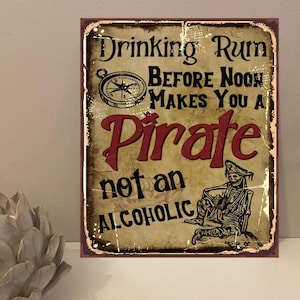 Peut inclure: Panneau métallique de style vintage avec le texte "Drinking Rum Before Noon Makes You A Pirate not an Alcoholic". Le panneau présente une boussole, un squelette de pirate et une illustration de navire. Aspect vieilli.