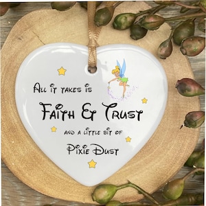 May include: White heart-shaped ceramic ornament with a Tinkerbell illustration and the text "All it takes is Faith & Trust and a little bit of Pixie Dust".