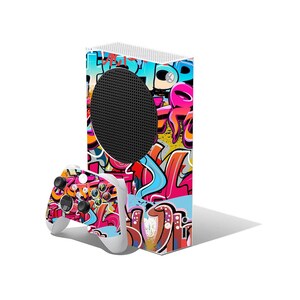May include: A white Xbox Series S console and controller with a vibrant graffiti-style design. The console features a black circular vent and is covered in colorful spray-painted art with pink, blue, and orange hues. The controller has matching graffiti art.