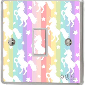 Op de afbeelding: Een lichtschakelaar-afdekplaat met een regenboog- en wit unicorn-patroon. De achtergrond is een pastel regenboog met witte sterren. De tekst "The Grafix Studio" staat in de rechterbenedenhoek.