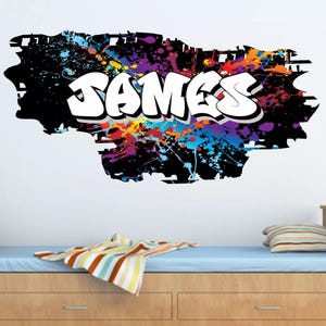 Pode incluir: Um adesivo de parede preto e branco com respingos de tinta coloridos e a palavra "JAMES" em fonte de graffiti branca.