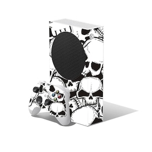 Könnte beinhalten: Ein weißes Spielkonsolen- und Controller-Set mit einem schwarz-weißen Totenkopfmuster. Die Konsole hat eine schwarze runde Lüftungsöffnung und der Controller hat farbige Tasten.