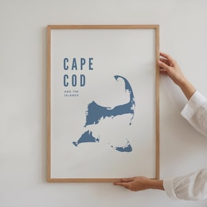 Może przedstawiać: Oprawiony wydruk z niebieską mapą Cape Cod i Wysp na białym tle. Słowa "CAPE COD AND THE ISLANDS" są wydrukowane na niebiesko u góry. Rama wykonana jest z jasnego drewna.
