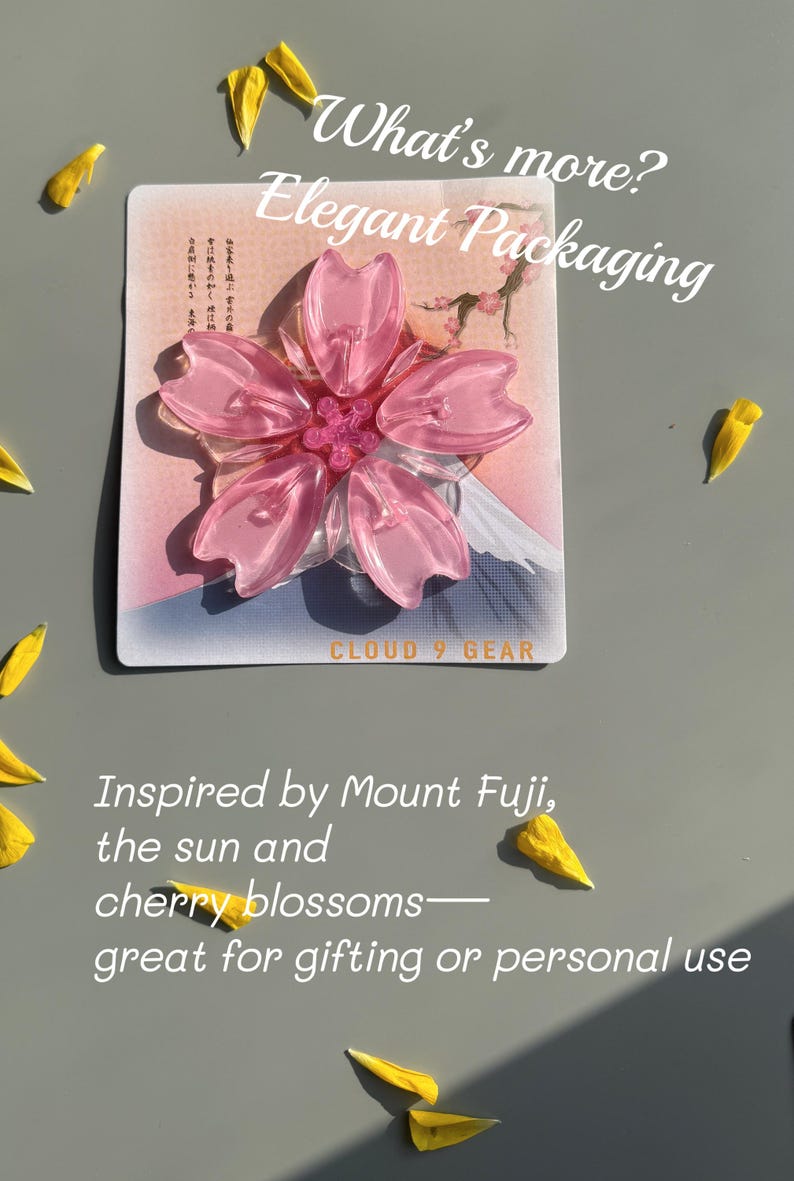 May include: A pink cherry blossom-shaped accessory on a card with text that reads "What's more? Elegant Packaging." The design is inspired by Mount Fuji and cherry blossoms. Yellow petals are scattered around.