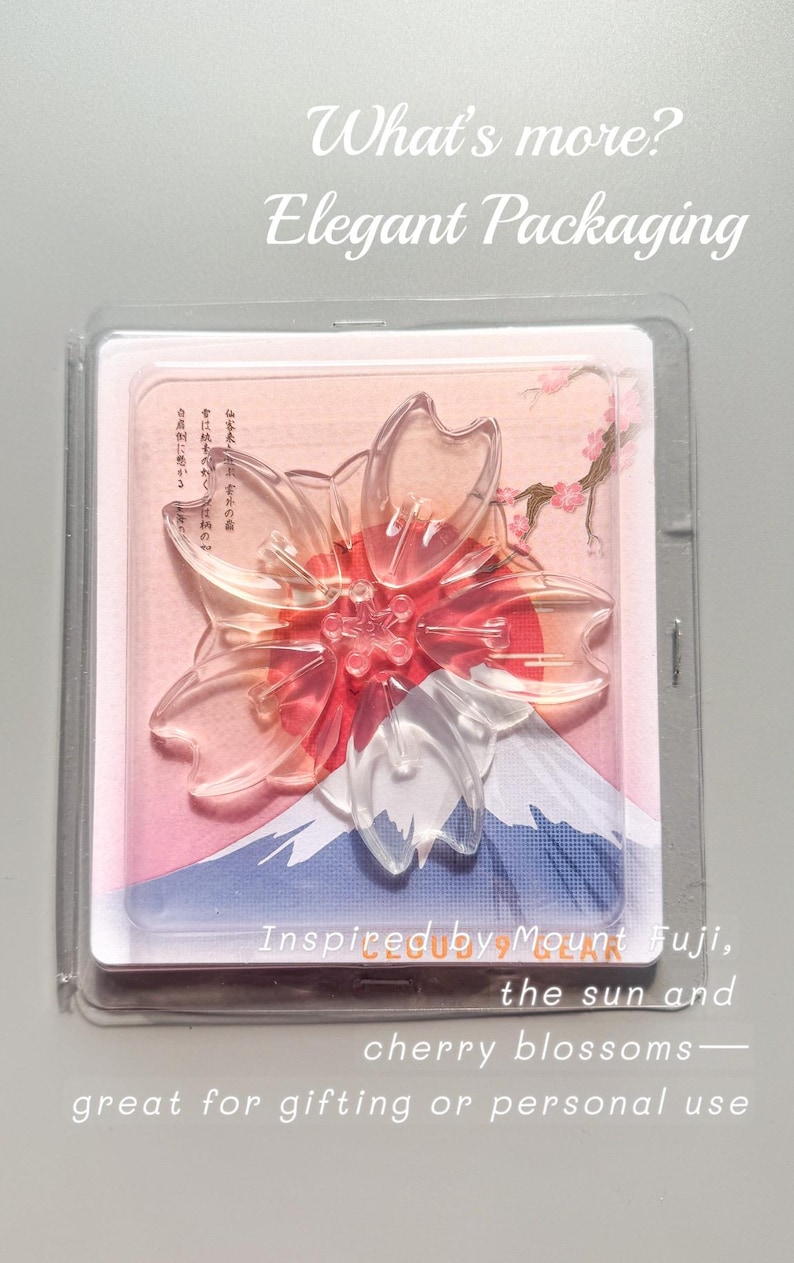 May include: Clear, transparent cherry blossom-shaped object with red accents, packaged in a clear plastic case. The packaging features a Mount Fuji illustration and text that reads "Inspired by Mount Fuji, the sun and cherry blossoms".
