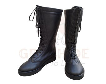 Könnte beinhalten: Ein Paar schwarze, kniehohe Stiefel mit Schnürdesign. Die Stiefel haben eine glatte, matte Oberfläche und eine runde Spitze. Die Schnürsenkel verlaufen über die Vorderseite der Stiefel, und die Sohlen sind flach.