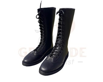 Könnte beinhalten: Ein Paar schwarze, kniehohe Stiefel mit Schnürung. Die Stiefel haben eine glatte, matte Oberfläche und eine runde Spitze. Die Schnürsenkel verlaufen über die Vorderseite der Stiefel. Die Sohlen sind dunkler.