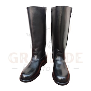 Puede incluir: Un par de botas altas de cuero negro. Las botas tienen un acabado liso y pulido y una cremallera en el lateral. Las botas son hasta la rodilla y tienen una puntera redondeada.
