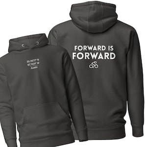 Pode incluir: Moletom cinza escuro com bolso frontal e capuz com cordão. A frente exibe as coordenadas 30.2672° N 97.7431° W, Austin. A parte de trás apresenta o texto "FORWARD IS FORWARD" com um gráfico de bicicleta.