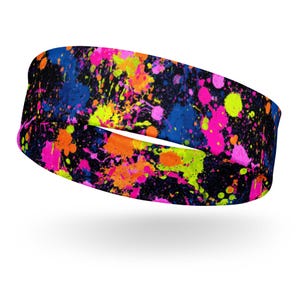 Puede incluir: Una diadema negra con un vibrante diseño de pintura salpicada. Las salpicaduras de pintura son de color rosa neón, naranja, amarillo y azul. La diadema es una banda ancha y elástica.
