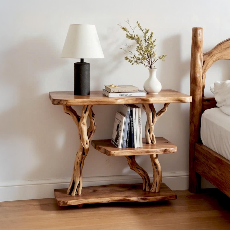 May include: A rustic wooden side table with a natural tree branch design. The table has two shelves and is supporting a lamp, books, and a vase with greenery. The wood has a warm, natural finish.