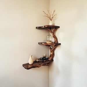 Puede incluir: Una estantería de esquina de madera con forma de árbol con tres estantes. La estantería está decorada con un pequeño jarrón con ramas secas, un frasco de vidrio y una pequeña botella.