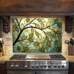 May include: A decorative kitchen backsplash featuring a stained glass design of a tree branch with leaves. The leaves are various shades of green and yellow against a light green and yellow background. The backsplash is installed above a stainless steel gas range.