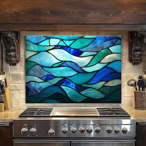 May include: A stained glass kitchen backsplash featuring an abstract design of ocean waves in shades of blue and teal. The artwork is installed above a stainless steel gas range, adding a decorative element to the kitchen.