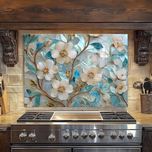 May include: A decorative kitchen backsplash featuring a floral design. The artwork showcases white flowers with gold centers, blue leaves, and brown stems against a light blue and white background. The backsplash is installed above a stainless steel gas range.