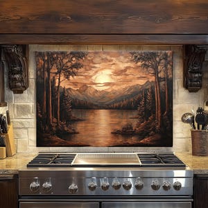 May include: A landscape painting depicting a serene lake scene with mountains, trees, and a sunset. The artwork is displayed above a stainless steel gas range in a kitchen setting. The color palette features warm tones of brown, orange, and gold.
