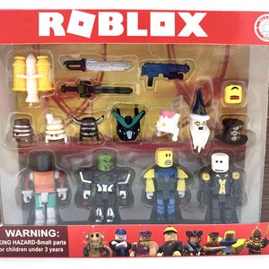 Może przedstawiać: Zestaw zabawek Roblox w przezroczystym plastikowym opakowaniu. Zestaw zawiera kilka figurek i akcesoriów, takich jak broń i kapelusze. Figurki są w różnych kolorach i wzorach. Opakowanie zawiera logo Roblox i ostrzeżenie o małych częściach.
