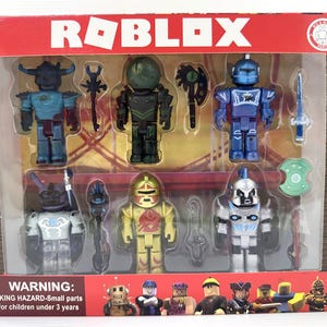 Może przedstawiać: Zestaw figurek Roblox w pudełku. Figurki są w różnych kolorach, w tym niebieskim, zielonym i złotym, i są zaprojektowane zbrojami i bronią. Opakowanie zawiera logo Roblox i ostrzeżenie o małych częściach.