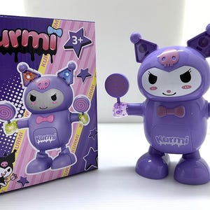 Op de afbeelding: Een paarse Kurumi speelgoedfiguur met bijpassende doos. De figuur heeft een schedelvormig hoofd, een strikje en houdt twee lolly's vast. De doos toont het Kurumi-personage en de tekst "Kurumi".
