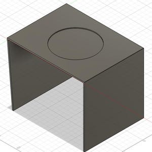 May include: A dark gray, geometric, open-sided box with a circular indentation on the top surface. The box is set against a grid background, and the design appears to be a 3D model or rendering.