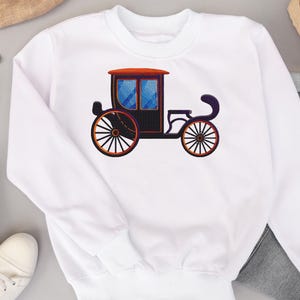 May include: White sweatshirt with a black carriage design. The carriage has a blue window and orange accents.