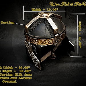 Peut inclure: Casque de guerre noir et doré, de 25,4 cm de large et 27,94 cm de haut. Il présente un moulage en laiton avec une armature en fer et un revêtement en cuir. Le texte "War Helmet For Warriors" est visible.