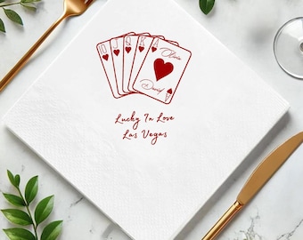 Op de afbeelding: Witte vierkante papieren servet met een rood speelkaartenontwerp. Het ontwerp bevat een tien, boer, vrouw, koning en een harten aas. De tekst "Lucky In Love Las Vegas" is eronder gedrukt.