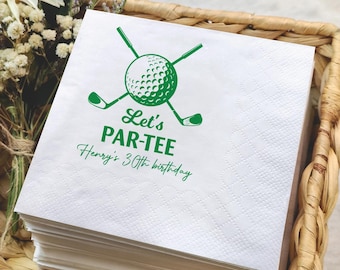 May include: A stack of white paper napkins with a green golf-themed design. The design includes a golf ball, crossed golf clubs, and the text "Let's PAR-TEE" and "Henry's 30th birthday". The napkins are in a woven basket.