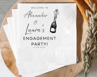 May include: White paper napkins with a diamond pattern, stacked on a wooden plate. The napkins feature the text "Welcome to Alexander & Laura's ENGAGEMENT PARTY! 10.08.2025" and a champagne bottle illustration.