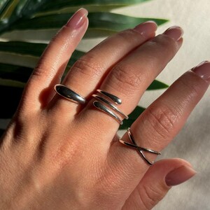 Könnte beinhalten: Drei silberne Ringe an einer Hand. Die Ringe sind alle in verschiedenen Stilen, einer ist ein einfaches Band, einer ist ein verdrehtes Band und der andere ist ein gebogenes Band.
