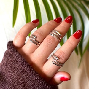 Könnte beinhalten: Ein Set aus drei silbernen Ringen mit einem einzigartigen, abstrakten Design. Die Ringe bestehen aus glattem, gebogenem Metall und werden am Zeige- und Mittelfinger getragen.