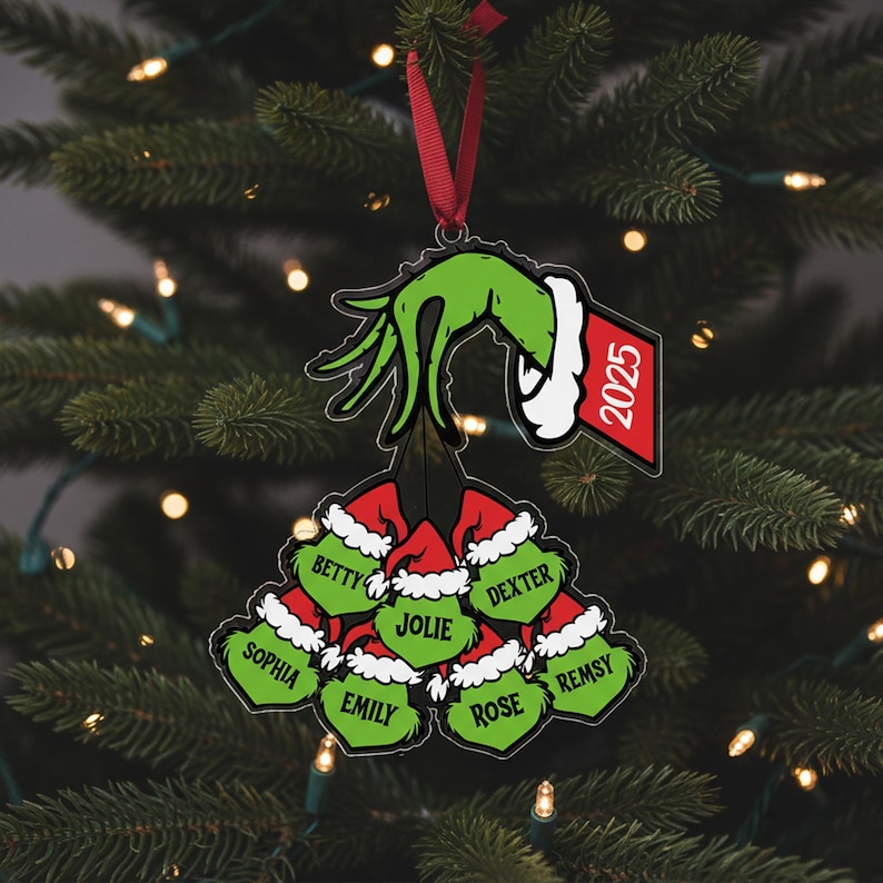 May include: A Christmas ornament featuring a green hand holding a cluster of red Santa hats, each with a name. The ornament has a red ribbon for hanging and a tag with the year 2025. The names include Betty, Dexter, Sophia, Emily, Jolie, Rose, and Remsy.