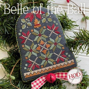 May include: A cross-stitch ornament featuring a bell with a red, green and orange floral design. The ornament is titled "Belle of the Ball" and is surrounded by green pine branches. The ornament is made by Hands On Design.