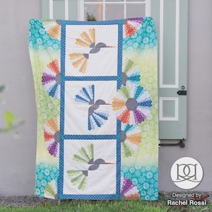 Peut inclure: Une courtepointe colorée avec un motif de colibri. La courtepointe présente un fond blanc avec trois panneaux carrés, chacun mettant en valeur un colibri. La courtepointe a une bordure bleue et est entourée d'un tissu vibrant à motifs. Le mot "Hover" est affiché en haut.