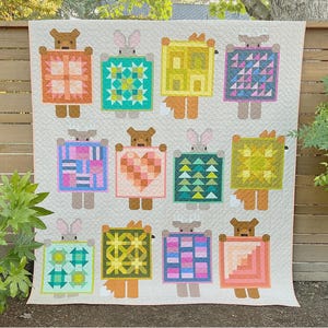 May include: A handmade quilt featuring whimsical animal figures holding colorful geometric designs. The quilt showcases a variety of colors, including pink, blue, yellow, and green, with a cream-colored background. The text "Show and Tell" is visible.