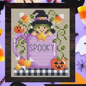 May include: Cross stitch pattern of a purple mug with the word "SPOOKY" on it. A witch with a green hat and dress is inside the mug. There are pumpkins and candy corn around the mug. The stitch count is 39w x 46h.