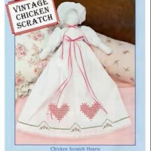 May include: A vintage-style pillowcase doll pattern for cross stitch and embroidery. The pattern features a white dress with pink hearts and a red ribbon. The doll is called "Vintage Chicken Scratch".