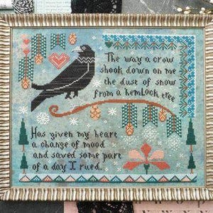 May include: Framed cross-stitch artwork featuring a black crow perched on a branch with text. The design includes a blue background, decorative borders, and a quote about a crow. The frame is gold-toned.