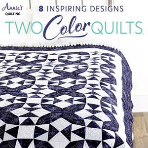 May include: A quilt with a geometric pattern in white and dark blue. The quilt is made with a variety of fabrics and has a quilted design. The quilt is folded in half and is lying on a white surface. The text "8 Inspiring Designs" and "Two Color Quilts" is visible on the cover.