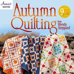 May include: A magazine cover featuring three colorful quilts with autumnal designs. The title of the magazine is "Autumn Quilting" with the subtitle "With Wendy Sheppard". The cover also features a bicycle with a basket of apples.