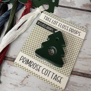 May include: A collection of craft supplies including green tree-shaped floss drops with various colored threads, a white snowflake, scissors, and a bottle brush tree. The floss drops card reads "Tree Lot Floss Drops" and "Primrose Cottage."