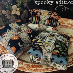 May include: Stacked fabric bundles with Halloween-themed patterns, including pumpkins and moons, are wrapped with decorative ribbon and a button closure. The text "That's A Wrap spooky edition" is visible.