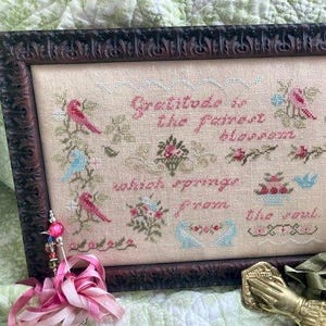 May include: A framed cross-stitch embroidery with a floral design and the text "Gratitude is the fairest blossom which springs from the soul".