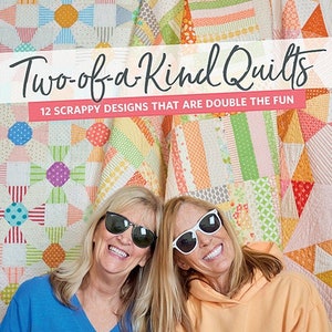 May include: Two women wearing sunglasses smile at the camera. They are standing in front of a colorful quilt with the title "Two-of-a-Kind Quilts" and the text "12 SCRAPPY DESIGNS THAT ARE DOUBLE THE FUN".