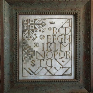 May include: A framed cross-stitch sampler with an alphabet design in brown thread on white fabric. The frame is distressed wood with a dark green finish. The sampler includes the text "Threadwork Primitives ©2021".