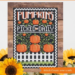 May include: Cross stitch pattern for a sign that says "Pumpkins Picked Daily". The sign is black with white lettering and a white picket fence. There are orange pumpkins with green vines on the sign. The stitch count is 64w x 88h.