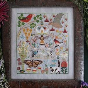 May include: A cross-stitch embroidery design featuring a beehive with a bee, a butterfly, birds, and flowers. The design is framed in a dark brown wood frame.